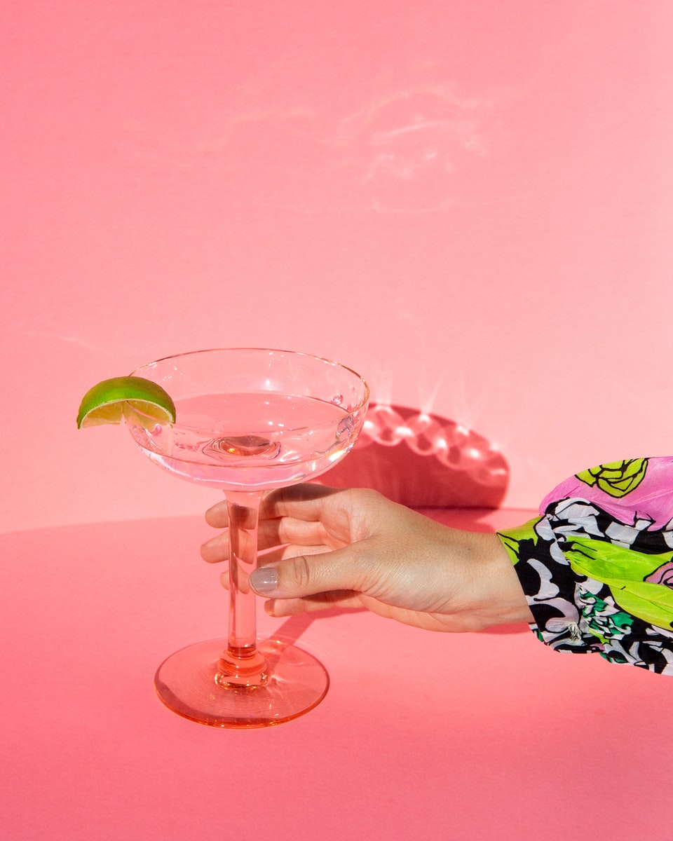 person holding clear wine glass with pink liquid